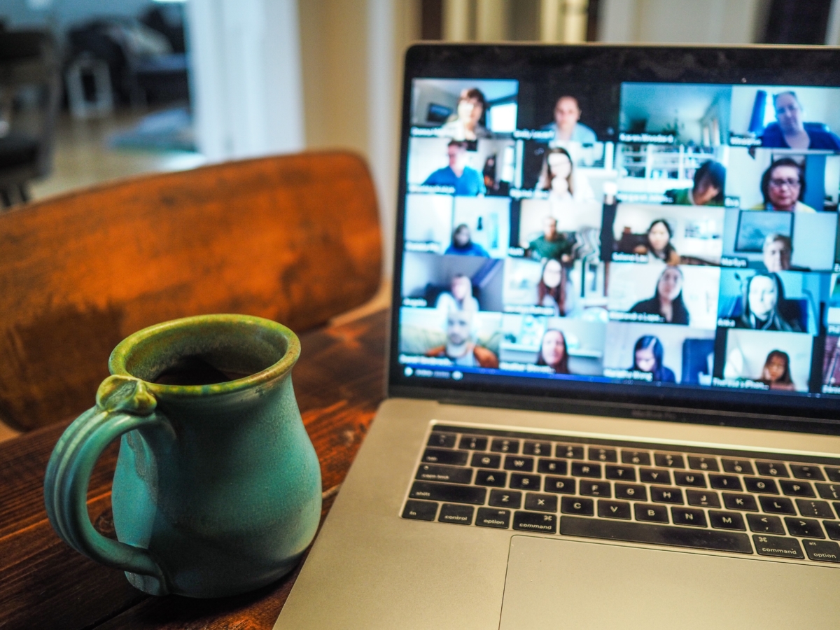 Image of an open laptop next to a cup of coffee. Laptop screen shows people's webcams on a video conference call